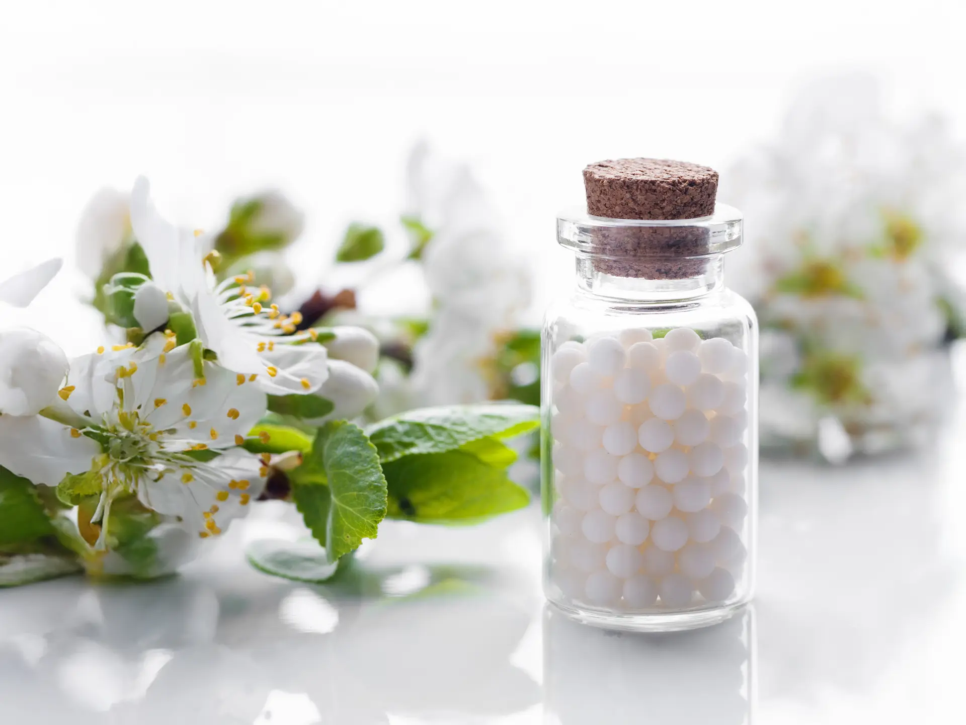 Glasfläschchen mit Globuli vor weißen Blüten